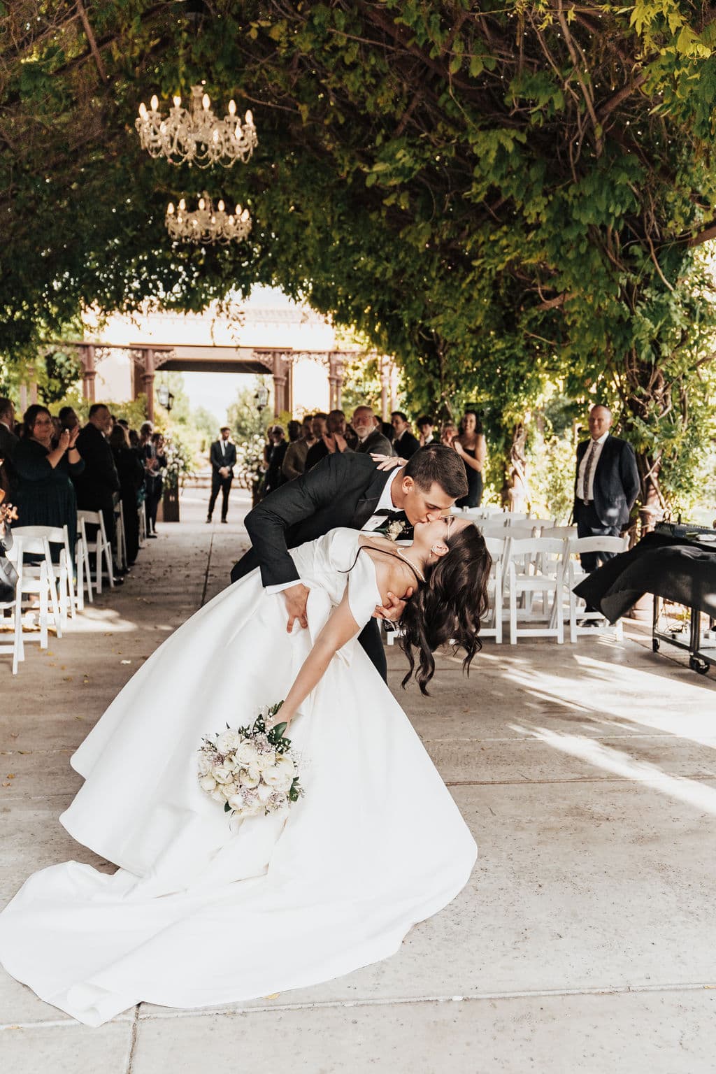 Real wedding photo — first kiss under a wisteria-covered pergola