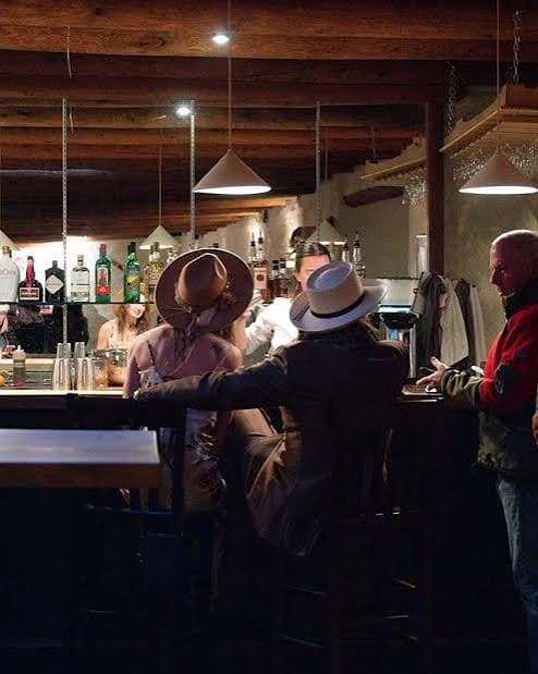 Guests gathered at the bar inside the rustic wood-beamed adobe interior at Saltos in Arroyo Seco